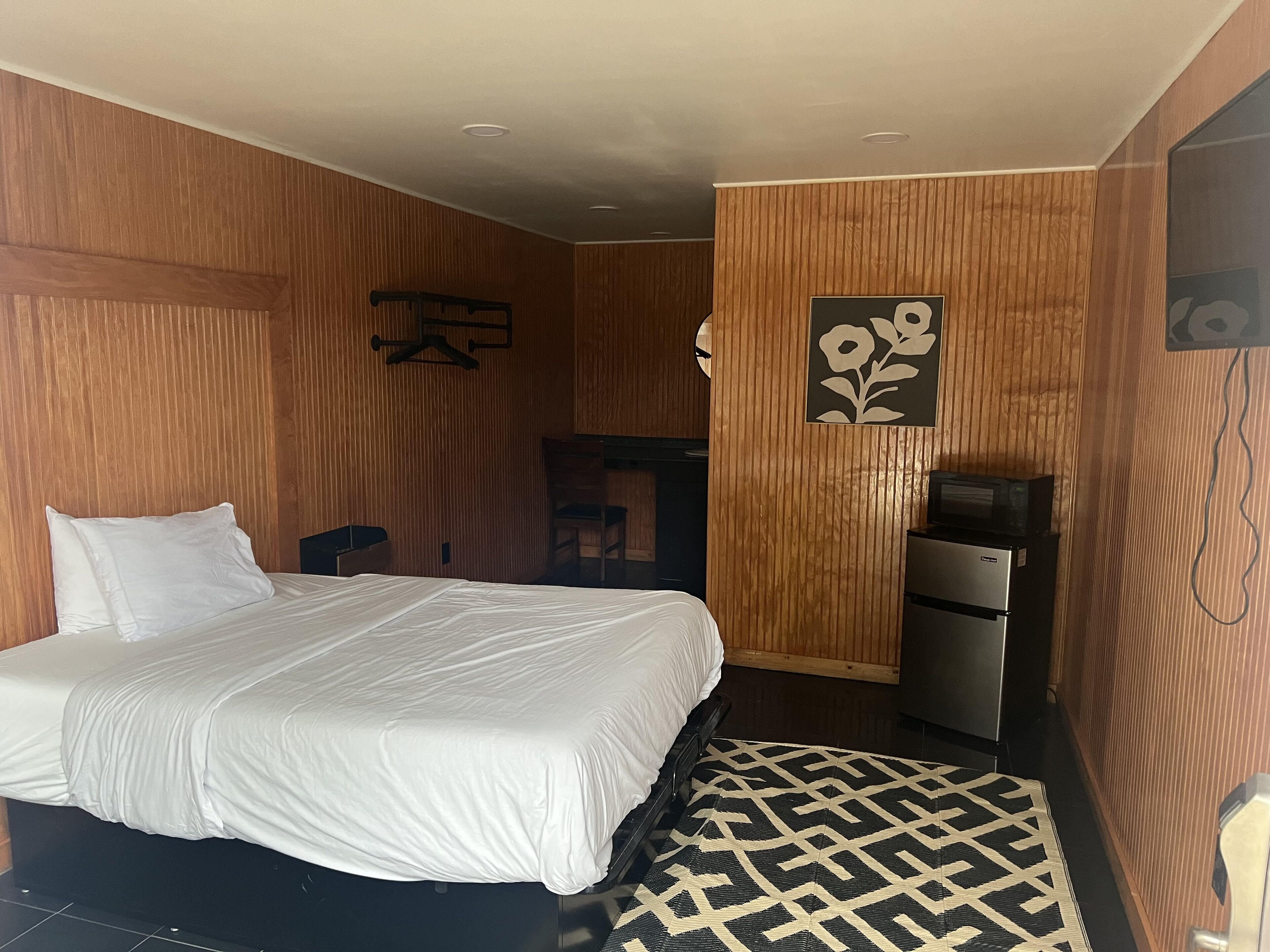 Quarto de hotel com uma cama grande, uma escrivaninha, uma cadeira, um guarda-roupa e uma televisão.