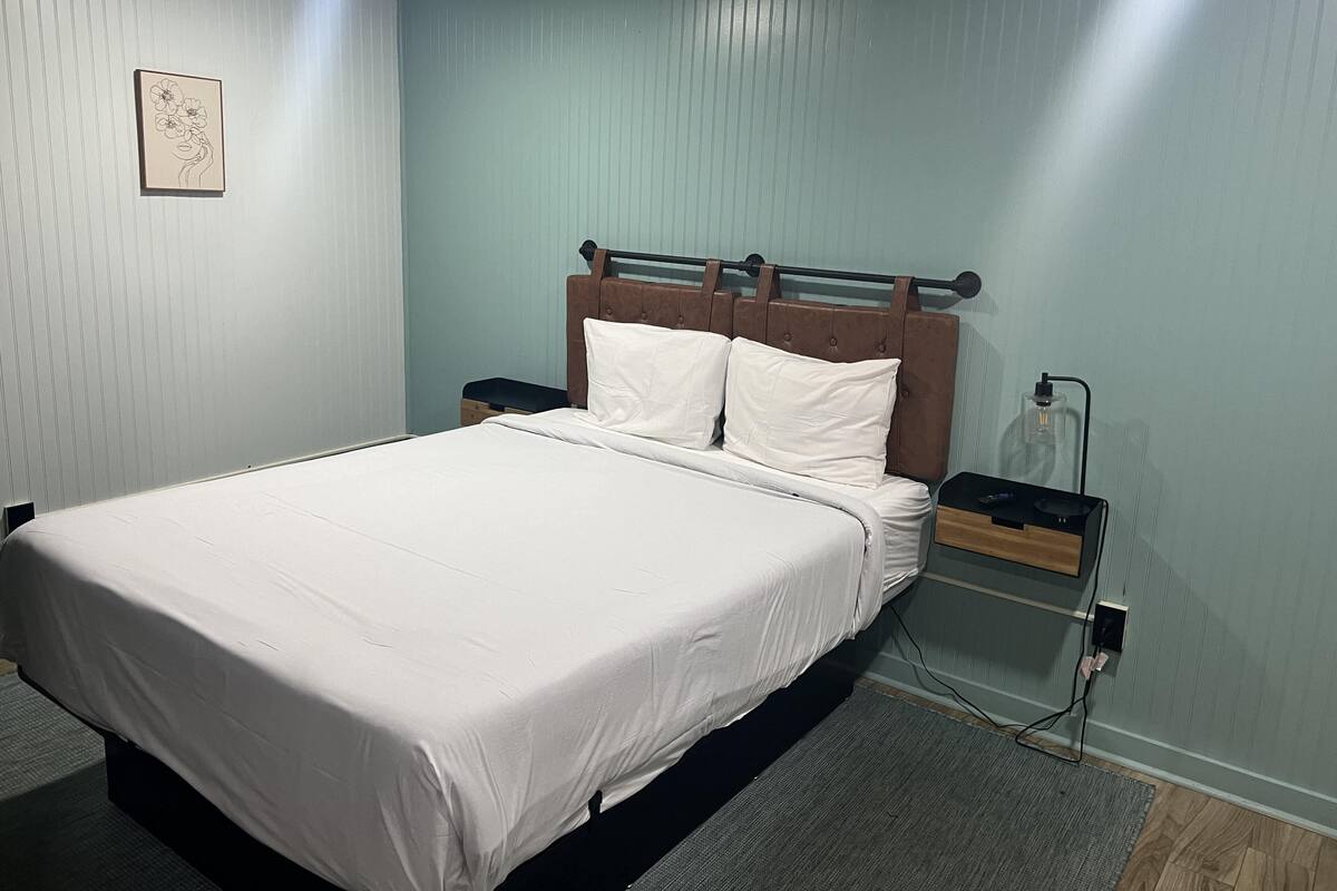 A neatly made bed with white linens, a wooden headboard, and a nightstand with a lamp.