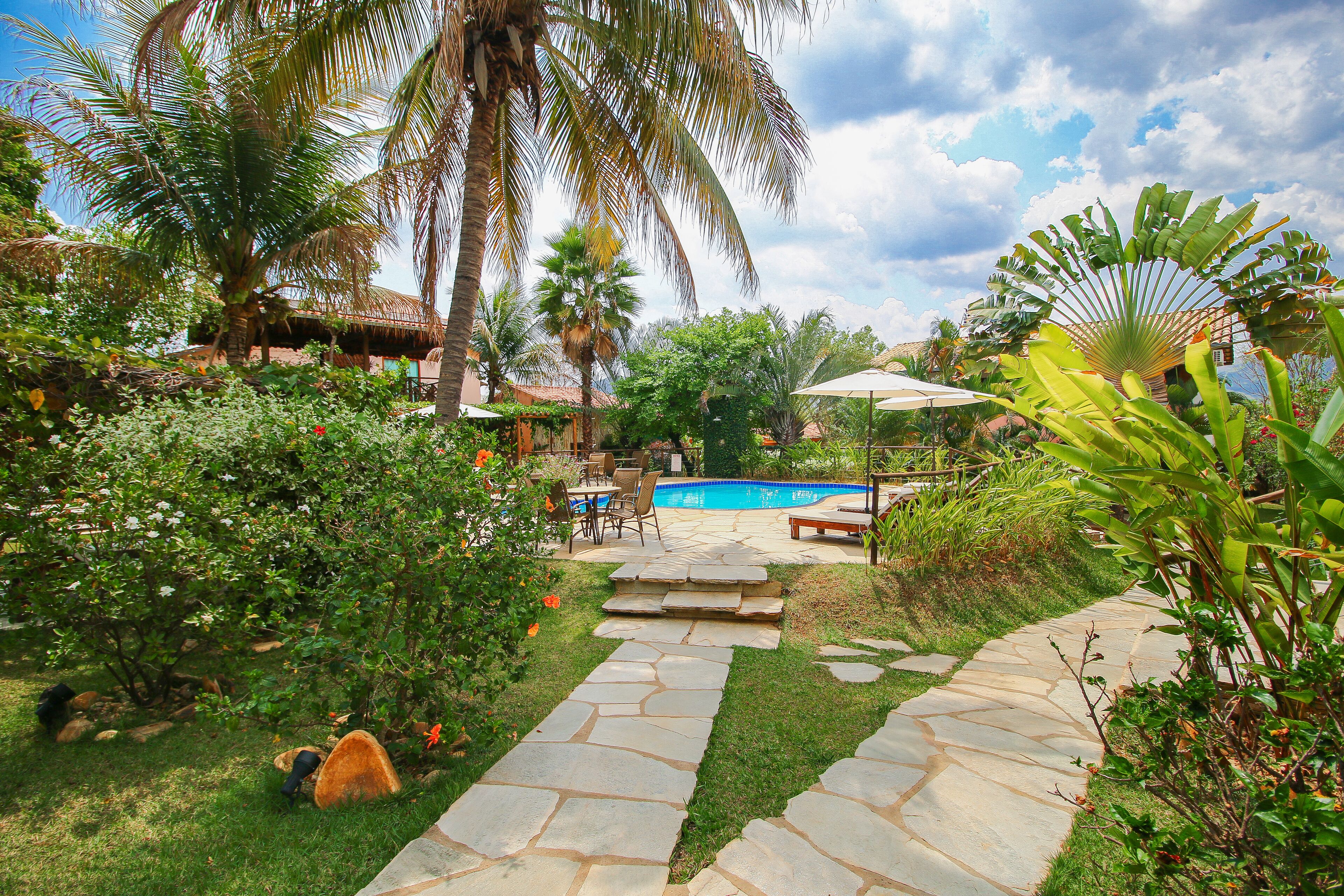 A backyard with a stone pathway, a pool, palm trees, and a thatched-roof structure.