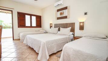 Quarto de hotel com três camas, uma janela grande com persianas de madeira, um aparelho de ar condicionado e uma luminária fixada na parede.