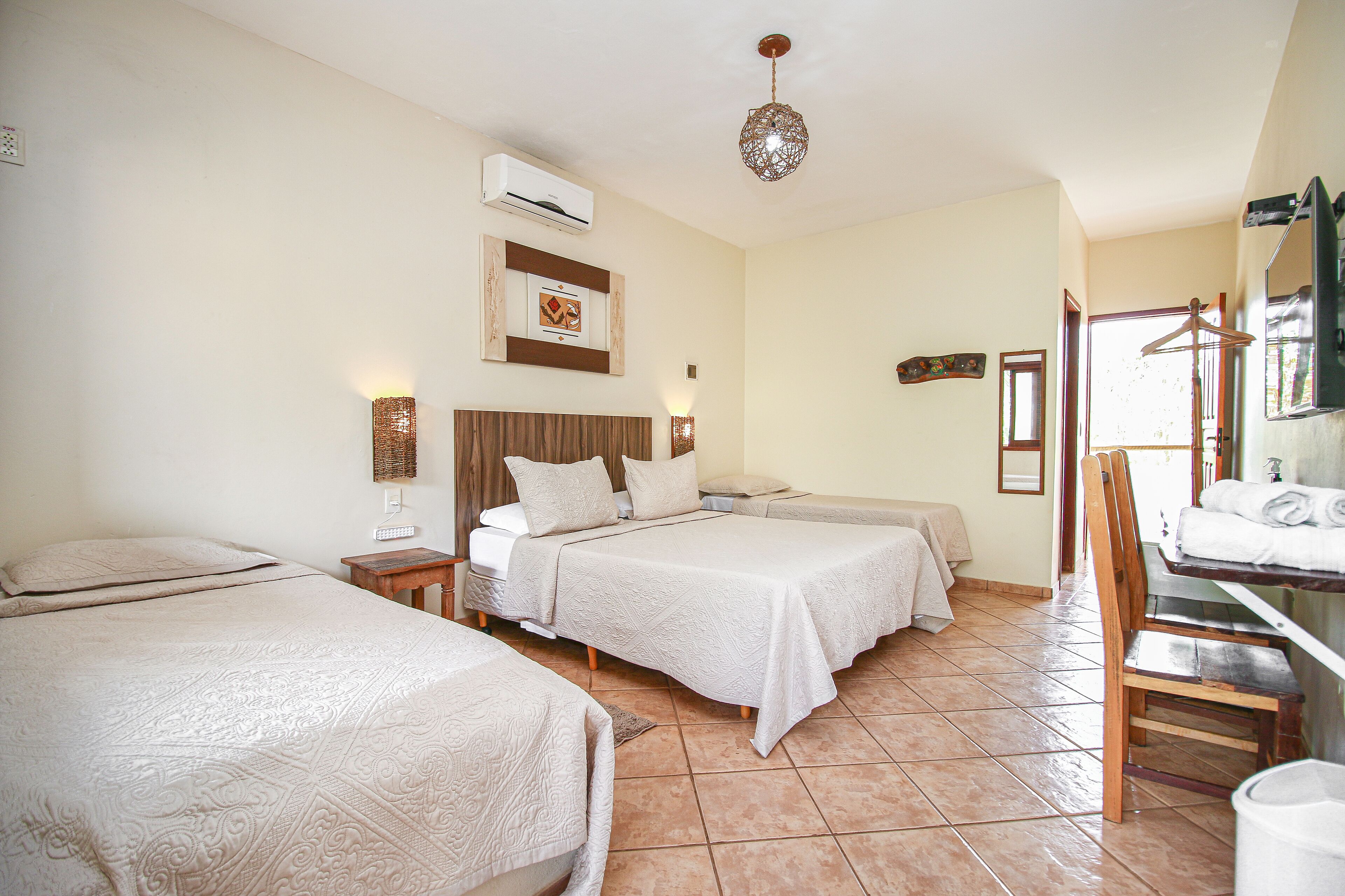 A hotel room with two beds, a wooden headboard, a bedside table with a lamp, and a bathroom with a towel rack and mirror.