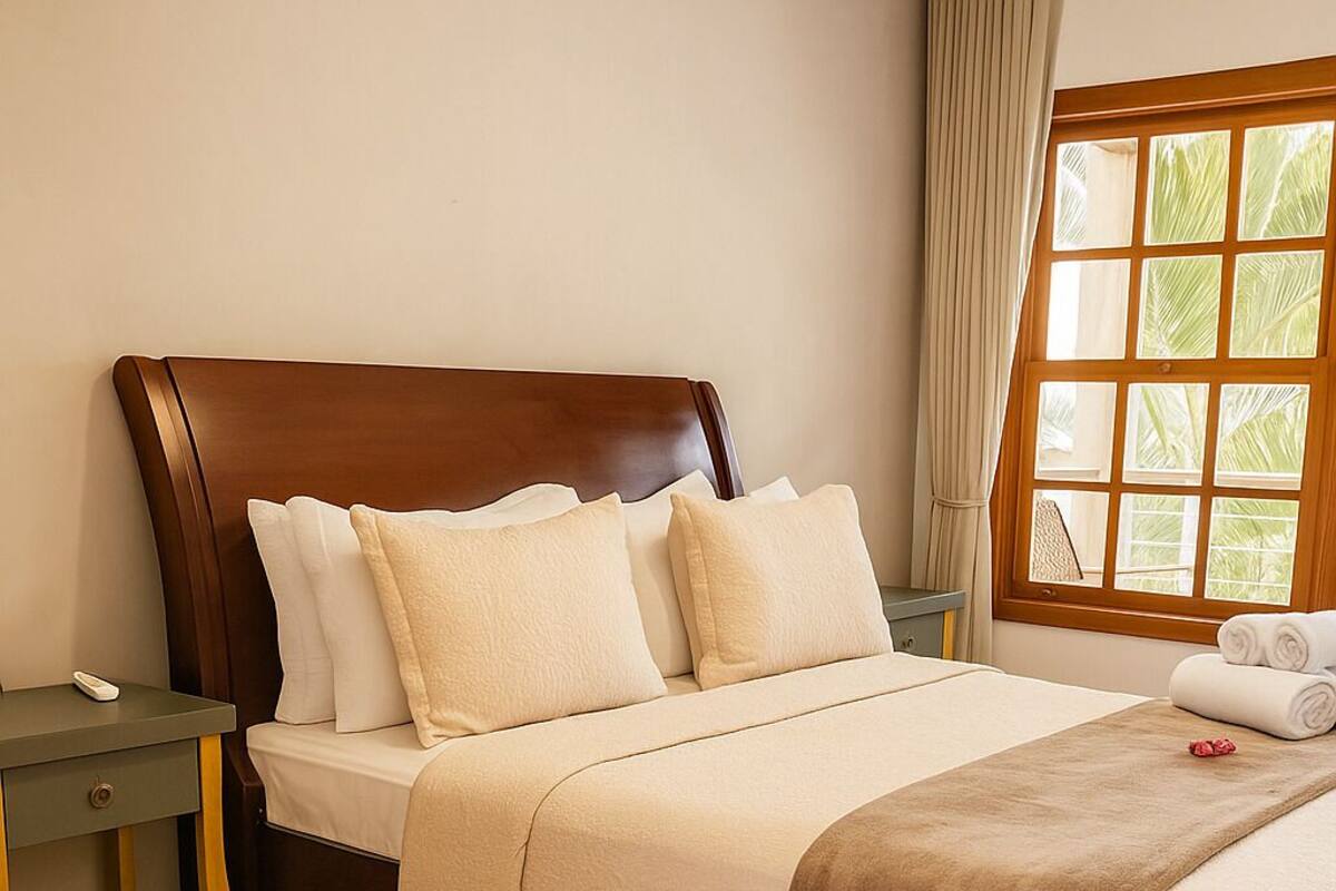 A hotel room with a large bed, a bedside table, a chair, and a window with curtains.