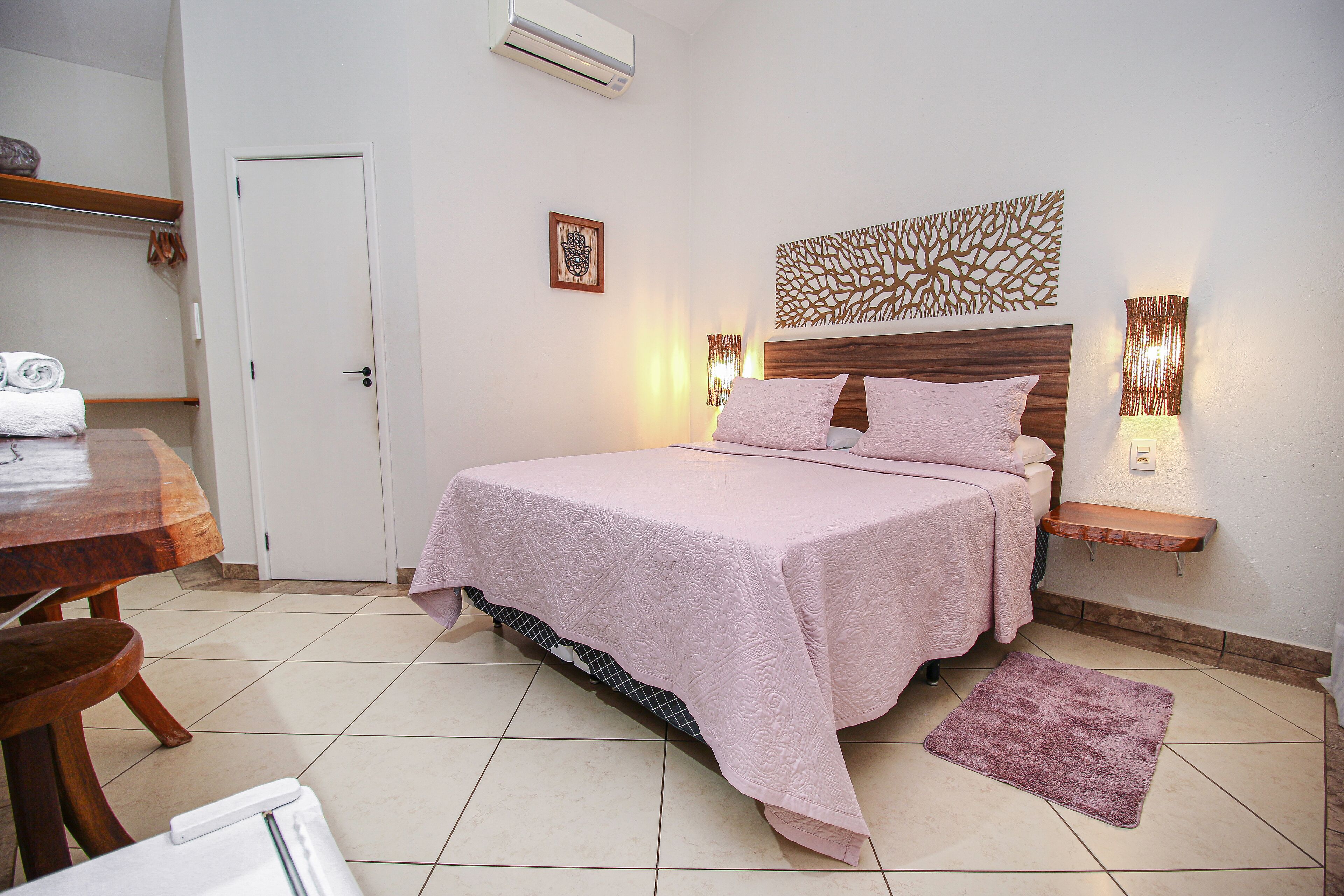 A neatly arranged bedroom with a bed, bedside tables, a wall-mounted air conditioner, and a small shelf.