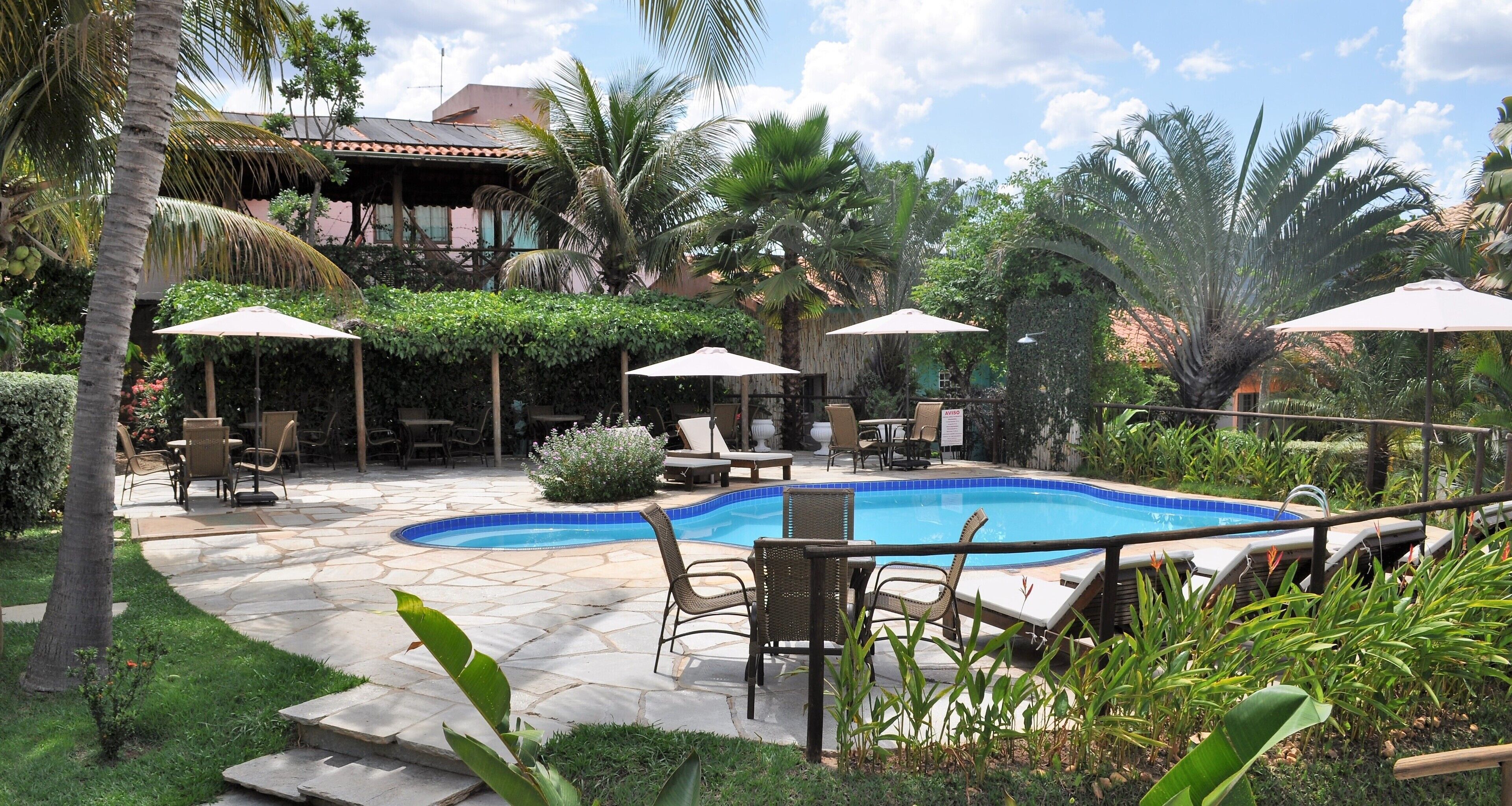 Un área de piscina con sillones de descanso y sombrillas, rodeada de exuberante vegetación y un patio de piedra.