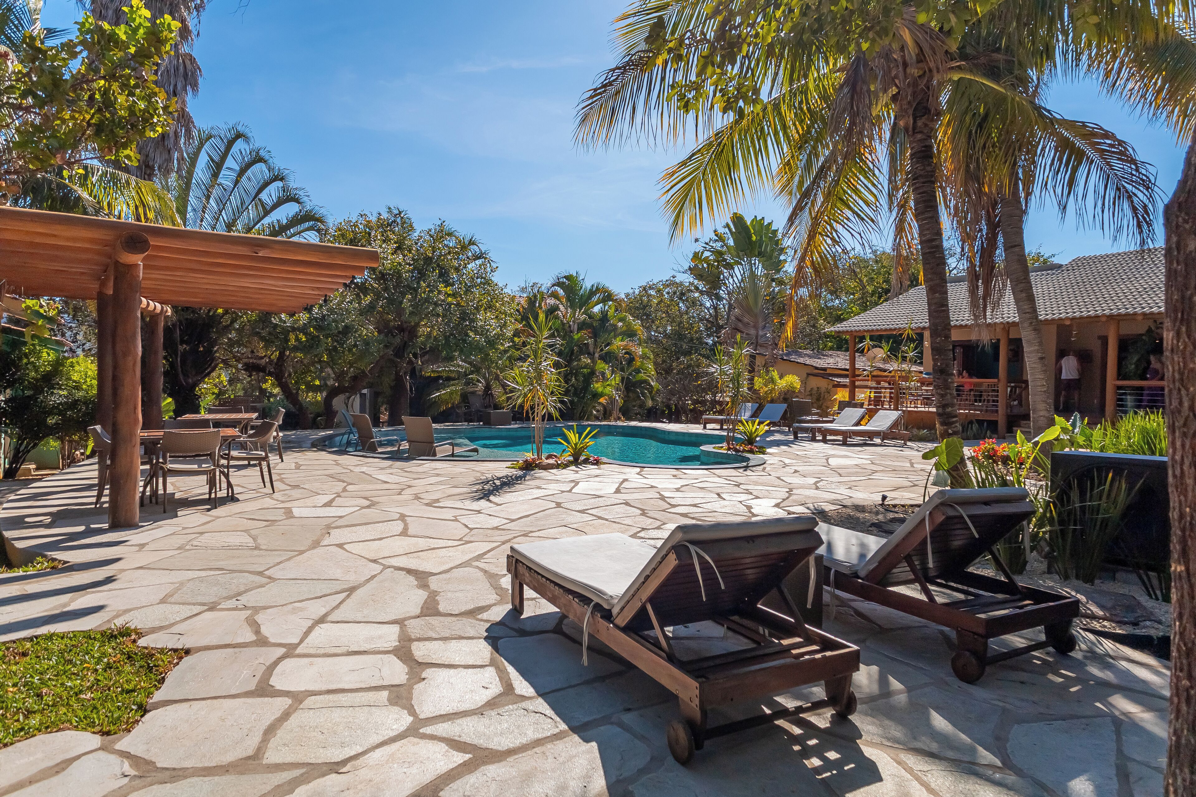 Un espace aménagé au bord de la piscine, avec des chaises longues, une pergola et une piscine.