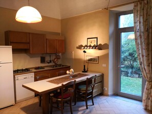 A kitchen with wooden cabinets, a white refrigerator, a dining table with chairs, and a view of the outdoors through a large window. - 19th century residence in Monferrato (Casale Monferrato)
