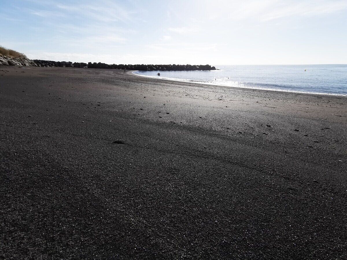 Une plage bordée d’une côte rocheuse, sous un ciel dégagé.