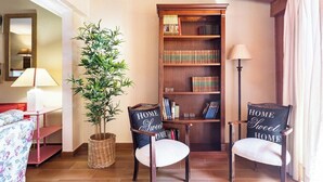 Ein gemütliches Wohnzimmer mit Bücherregal, zwei Sesseln mit 'HOME Sweet HOME' Kissen, einer Lampe und einem Blumentopf.