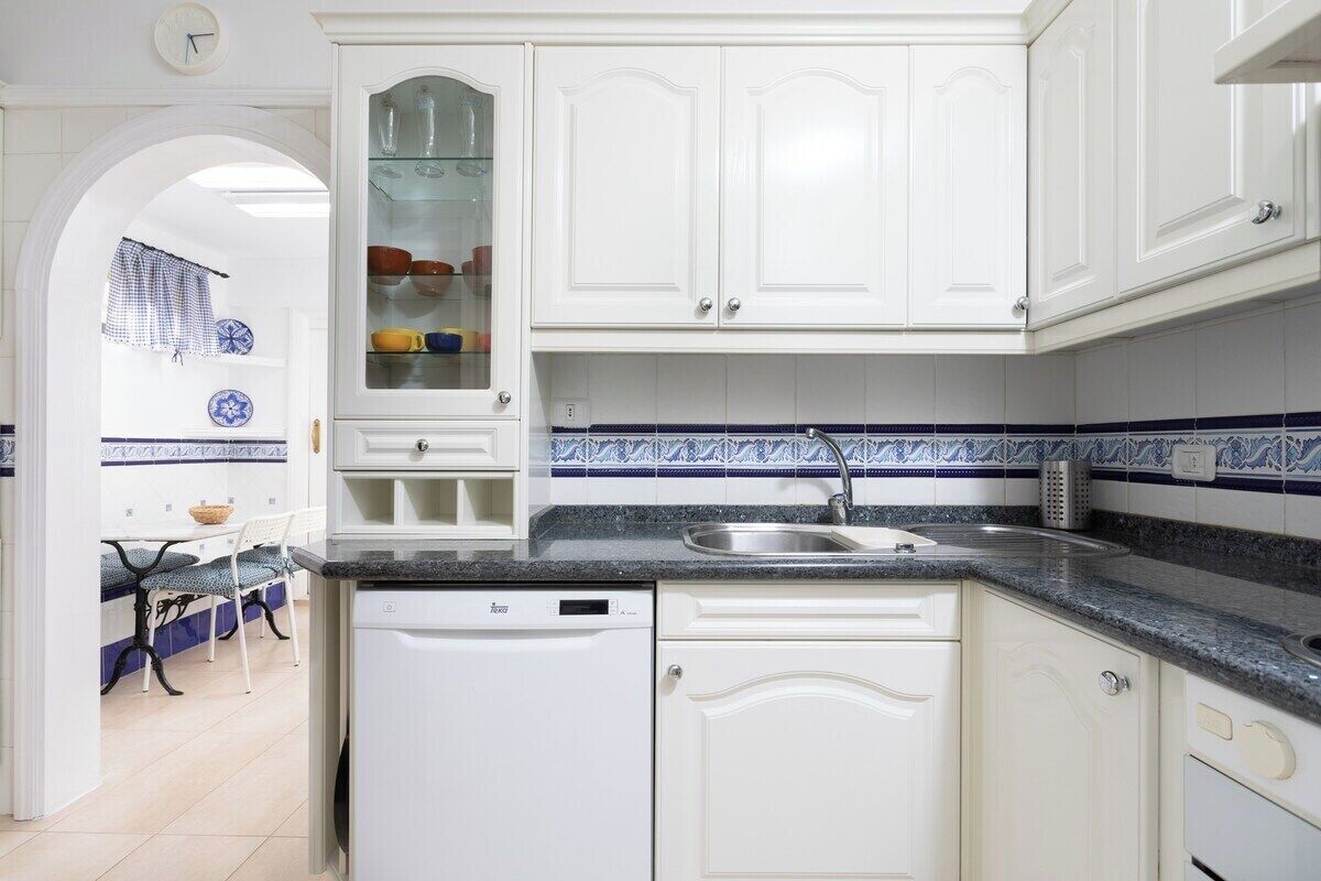 Una cocina con armarios blancos, lavavajillas, pileta y salpicadero de azulejos.
