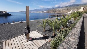 Ein Strand mit einer Holzterrasse, Palmen und einer felsigen Küstenlinie.