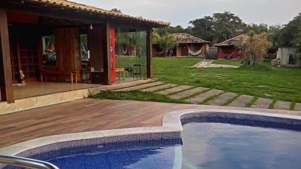 A swimming pool with two metal chairs, a wooden deck, and a covered area with a bench. - Pousada das Papoulas (Búzios)