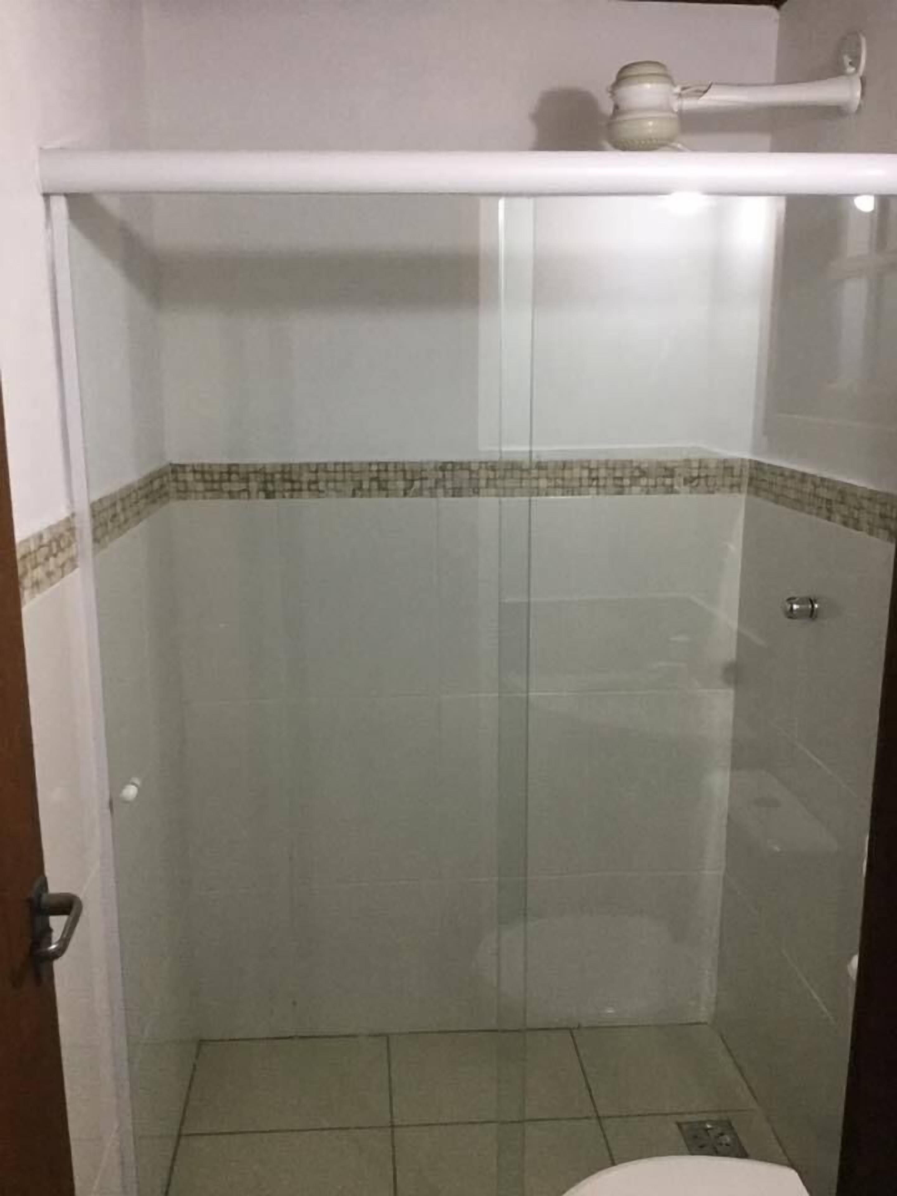 Un pequeño espacio de ducha cerrado con puerta de vidrio, un perchero blanco arriba y suelo de baldosas.