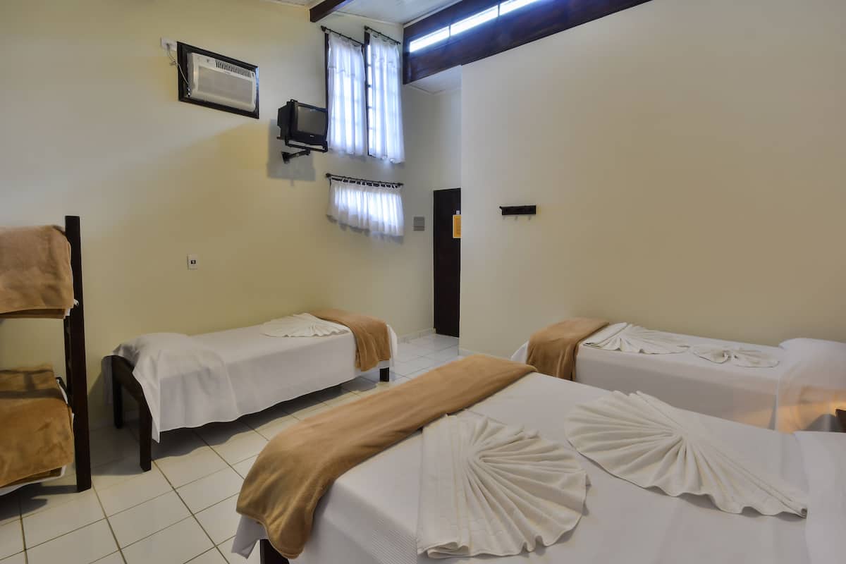 A hotel room with two single beds, a bench, a TV, and a window with curtains.