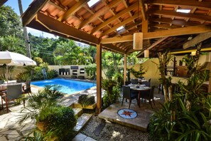 A covered outdoor area with a pool, dining table, chairs, and potted plants. - Pousada Estalagem Casa Grande (Ubatuba)