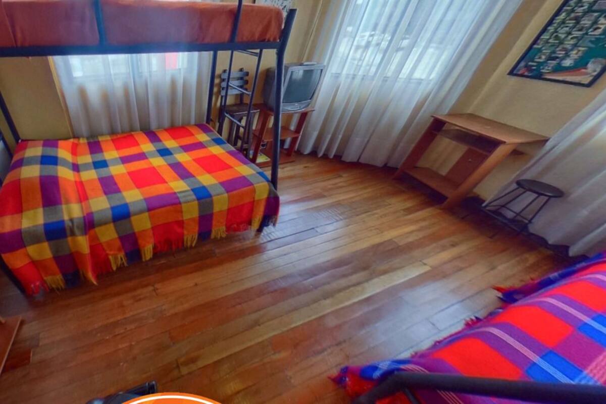 Ein Schlafsaalzimmer mit Etagenbetten, Holzboden, kleinem Tisch und Fernseher.