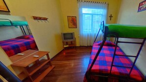 Un dormitorio con literas, una mesa de madera, un televisor y una ventana con cortinas.
