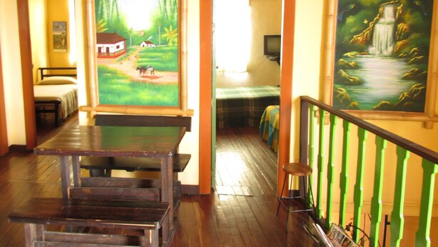 Una habitación con una mesa de madera, una cama con una colcha verde y un cuadro de una cascada.