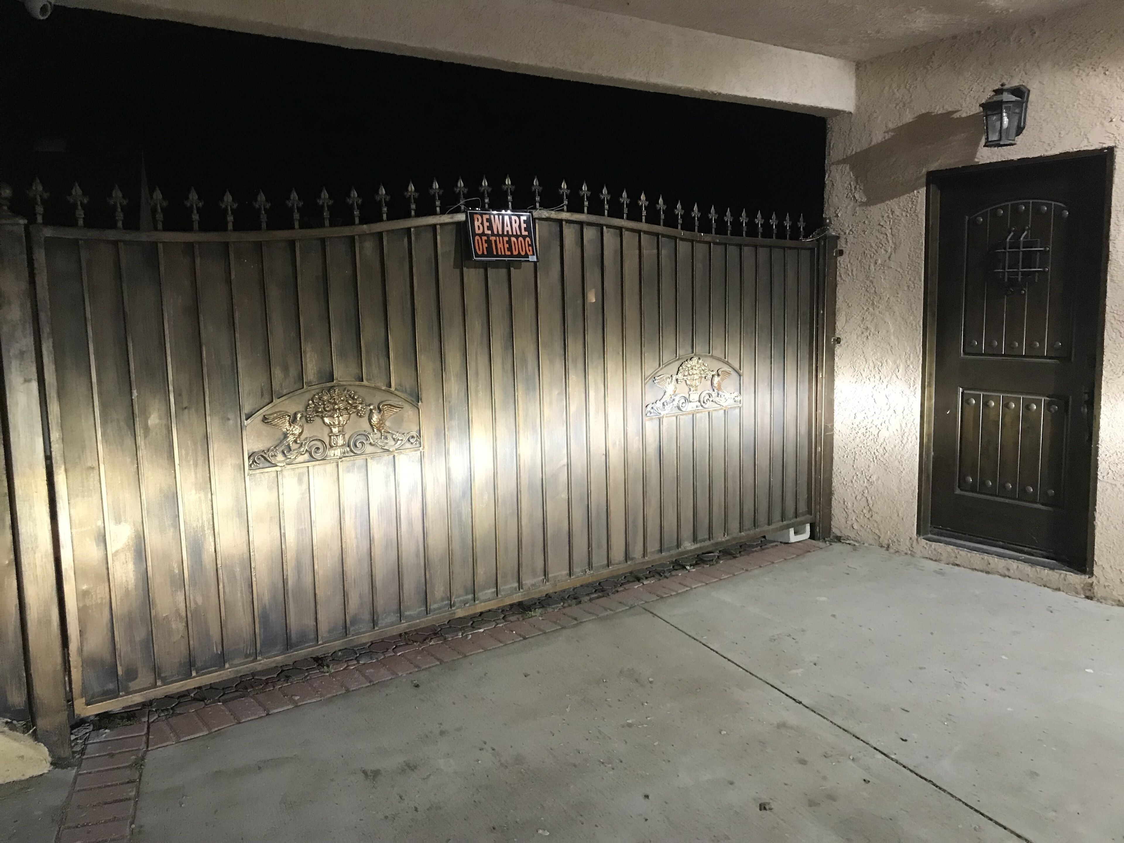 Une entrée fermée par un portail, agrémentée d’un panneau d’avertissement, d’un portail en métal décoratif et d’une porte dotée d’une fenêtre grillagée.