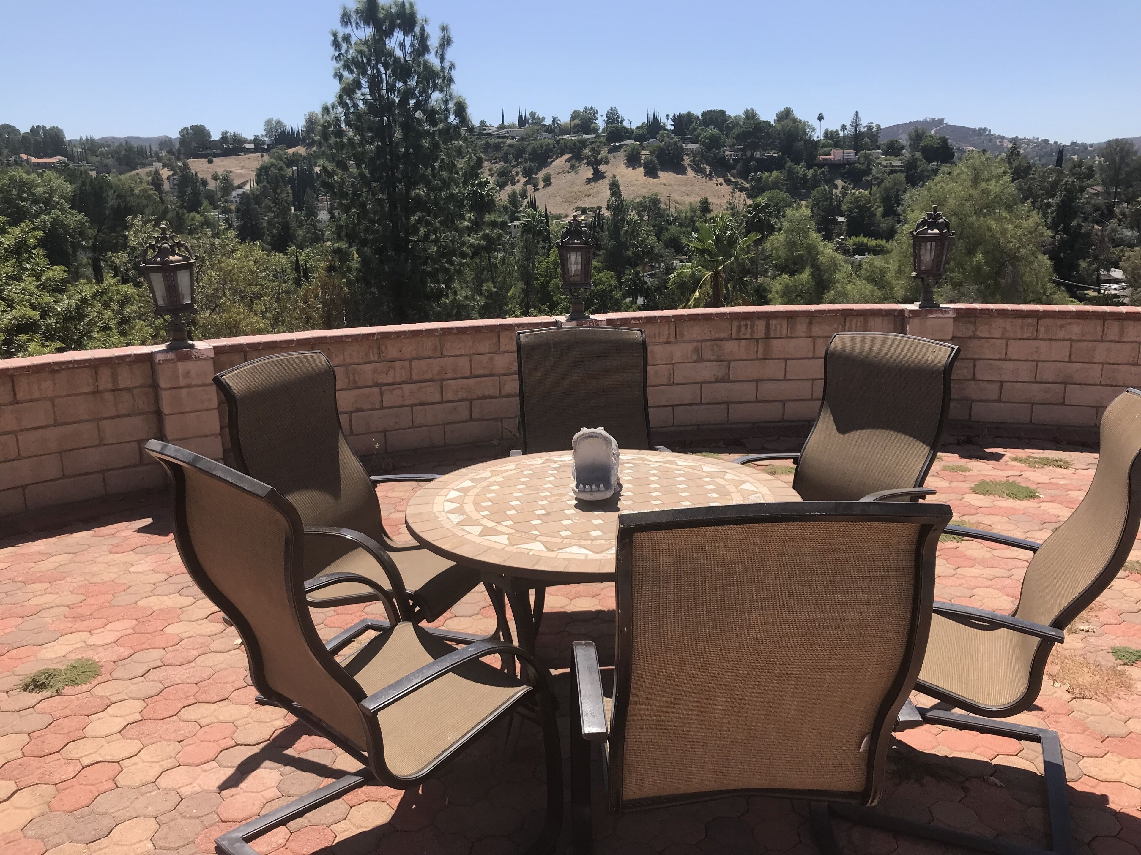 Un patio con una mesa redonda y sillas, un muro de ladrillo y vistas a un paisaje montañoso.