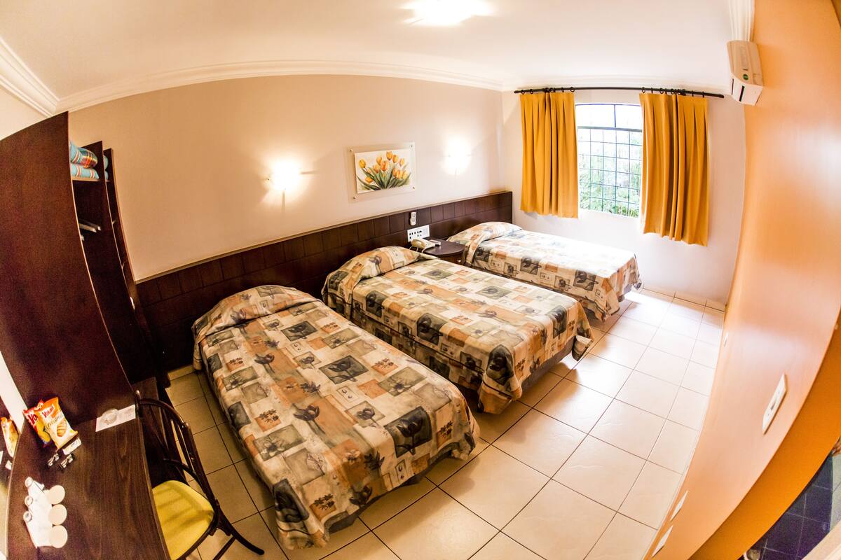 Une chambre d’hôtel avec deux lits, un bureau, une chaise et une fenêtre avec des rideaux.