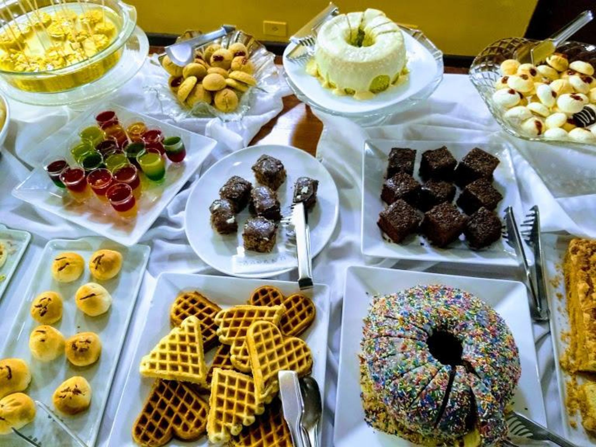 Uma mesa de buffet com diversos alimentos, incluindo waffles, um bolo e uma variedade de sobremesas.