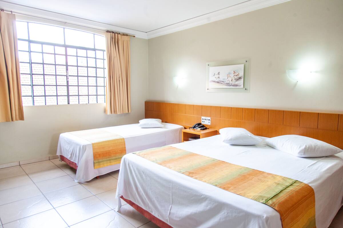 Une chambre d’hôtel avec deux lits, une fenêtre avec des rideaux, une table de chevet avec un téléphone et un luminaire fixé au mur.