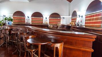 Uma área de bar com mobiliário de madeira, arcadas e cortinas listradas.