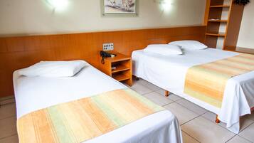 Habitación de hotel con dos camas individuales, una mesita de noche de madera con un teléfono, un cuadro en la pared y un armario con perchas.