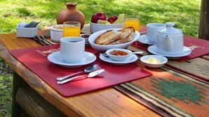 An outdoor breakfast setup with a table, breakfast items, and a view of a wooded area with cabins. - Paso del Cóndor (Nogolí)