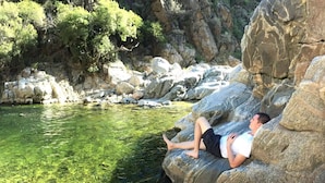 A person relaxing on a rock by a clear water body surrounded by rocky terrain and greenery. - Paso del Cóndor (Nogolí)