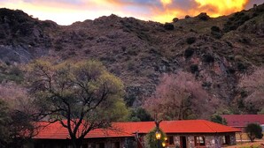 A rustic stone building with a red roof, surrounded by a red pathway and trees. - Paso del Cóndor (Nogolí)