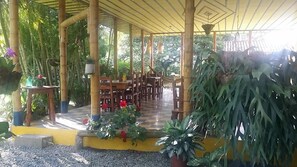 A covered outdoor seating area with wooden tables and chairs, surrounded by potted plants and greenery. - Finca Hotel El Barranco (Montenegro)