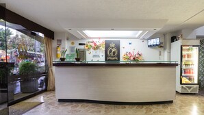 A hotel reception area with a glass partition, a reception desk, a mounted television, and a refrigerator stocked with beverages. - Ayenda 1234 Imperio 70 (Medellín)