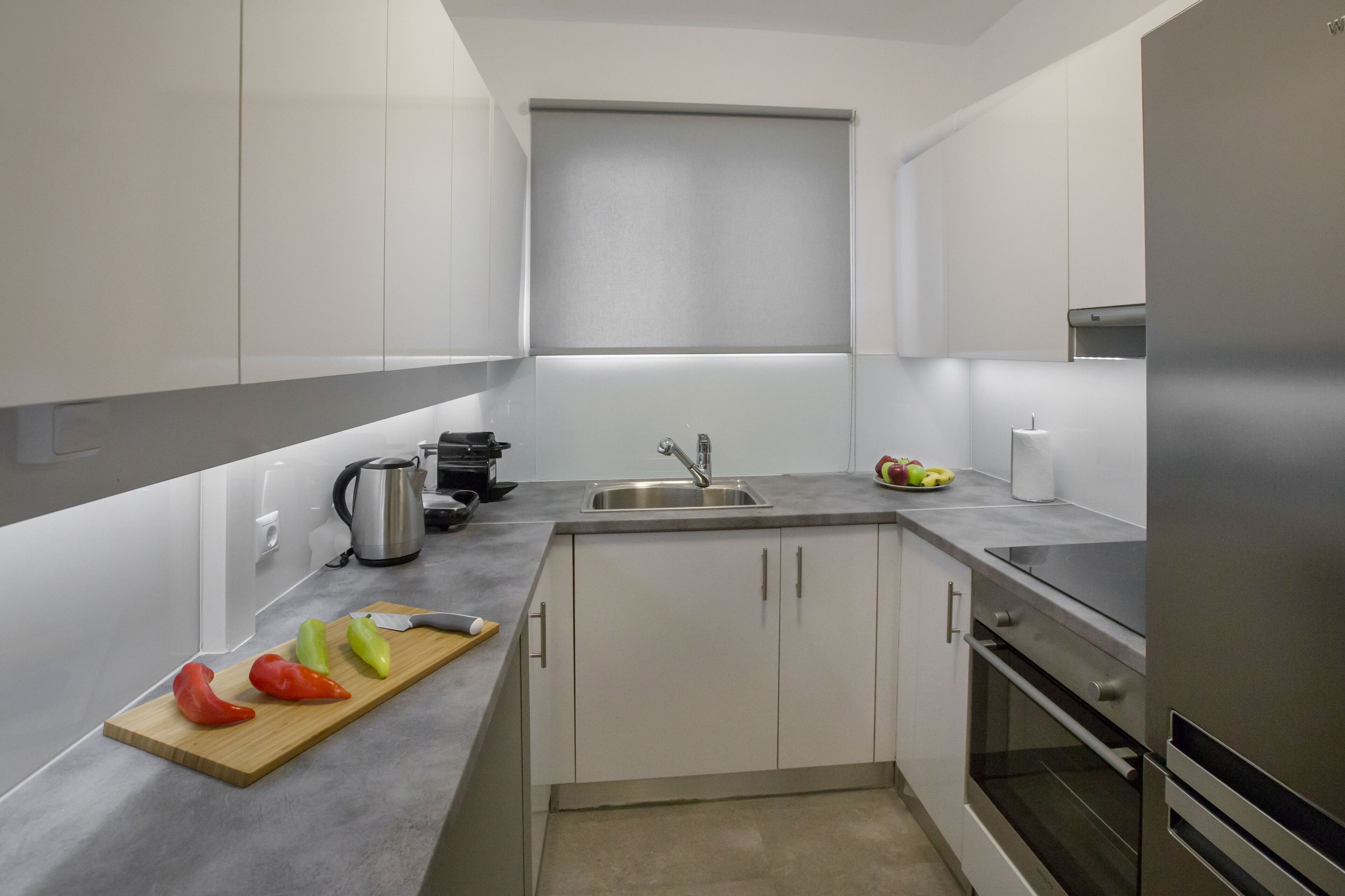 A modern kitchen with white cabinets, a stainless steel sink, and a built-in oven.