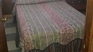 A bedroom with a checkered floor, a patterned bedspread, a nightstand with a lamp, and a window with a patterned curtain.
