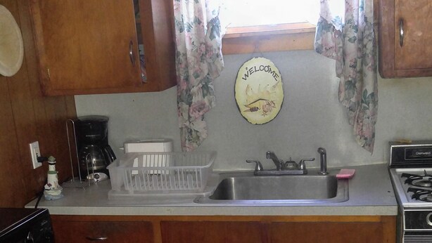 A kitchen with wooden cabinets, a sink, a stove, and a window with floral curtains.