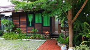Una casa de madera con un sendero de ladrillo rojo que lleva a la entrada, rodeada de exuberante follaje y plantas en macetas.