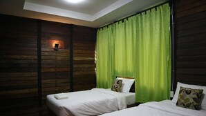 Habitación de hotel con dos camas, cortinas verdes, paneles de madera y una lámpara en el techo.
