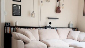 A living room with a beige sectional sofa, a patterned rug, a bookshelf, and wall-mounted light fixtures. - The Eureka: Four King Bedroom House (Champaign)