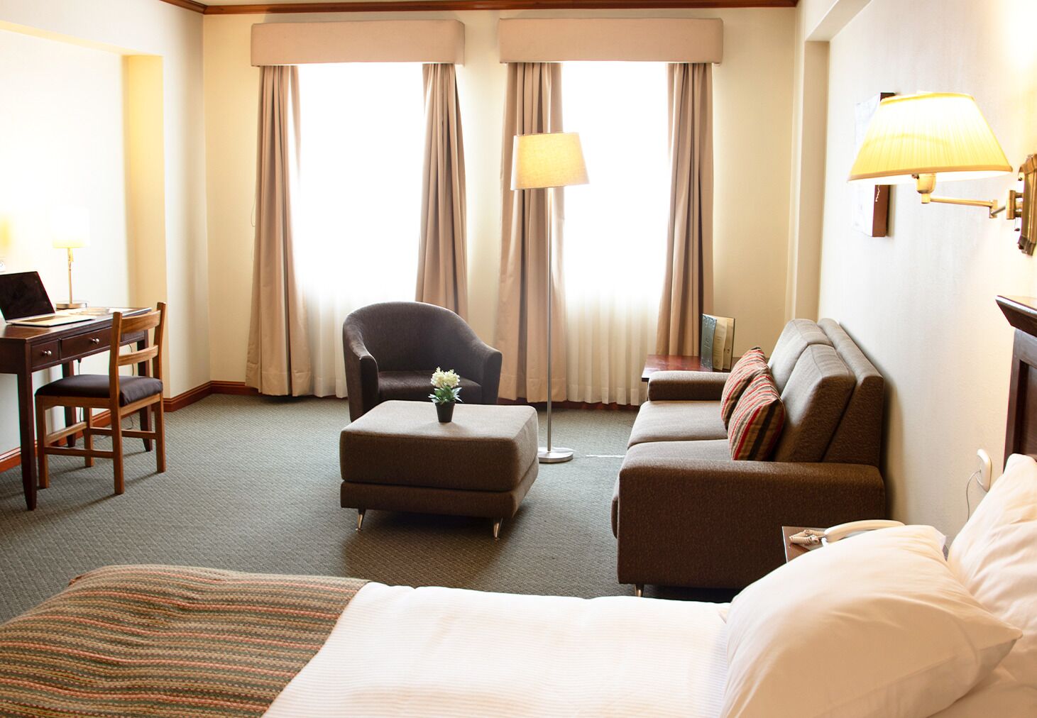 A hotel room with a bed, a sofa, a chair, a desk, and a lamp.