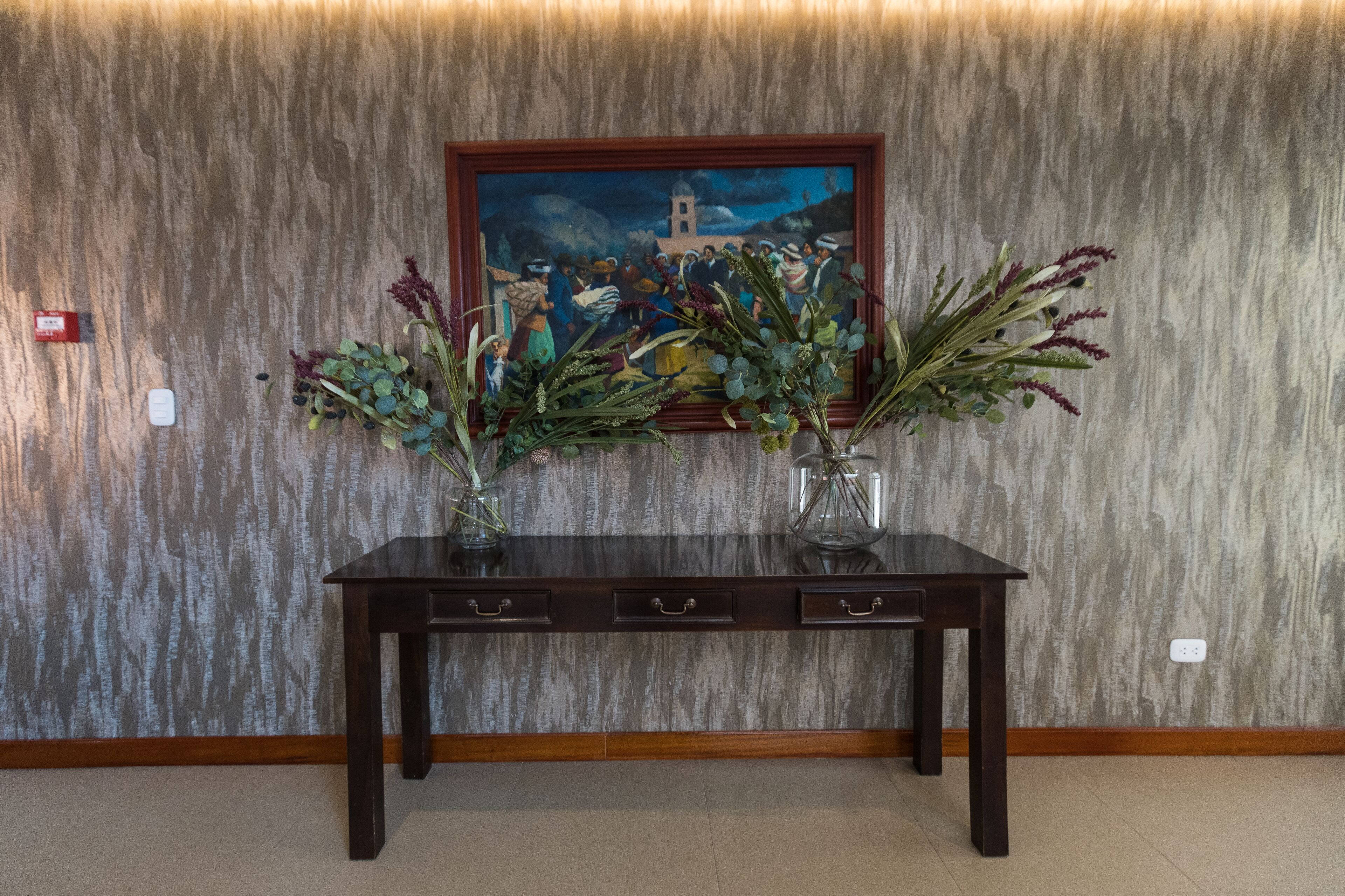 Una consola de madera con dos jarrones de plantas secas frente a una pared texturizada.
