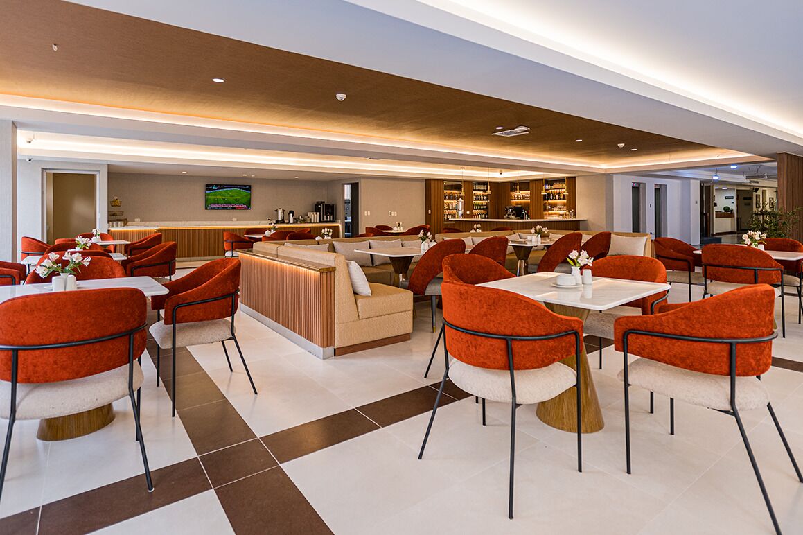 Una moderna hall d'albergo con poltrone imbottite rosse, tavoli bianchi e un'area bar sullo sfondo.