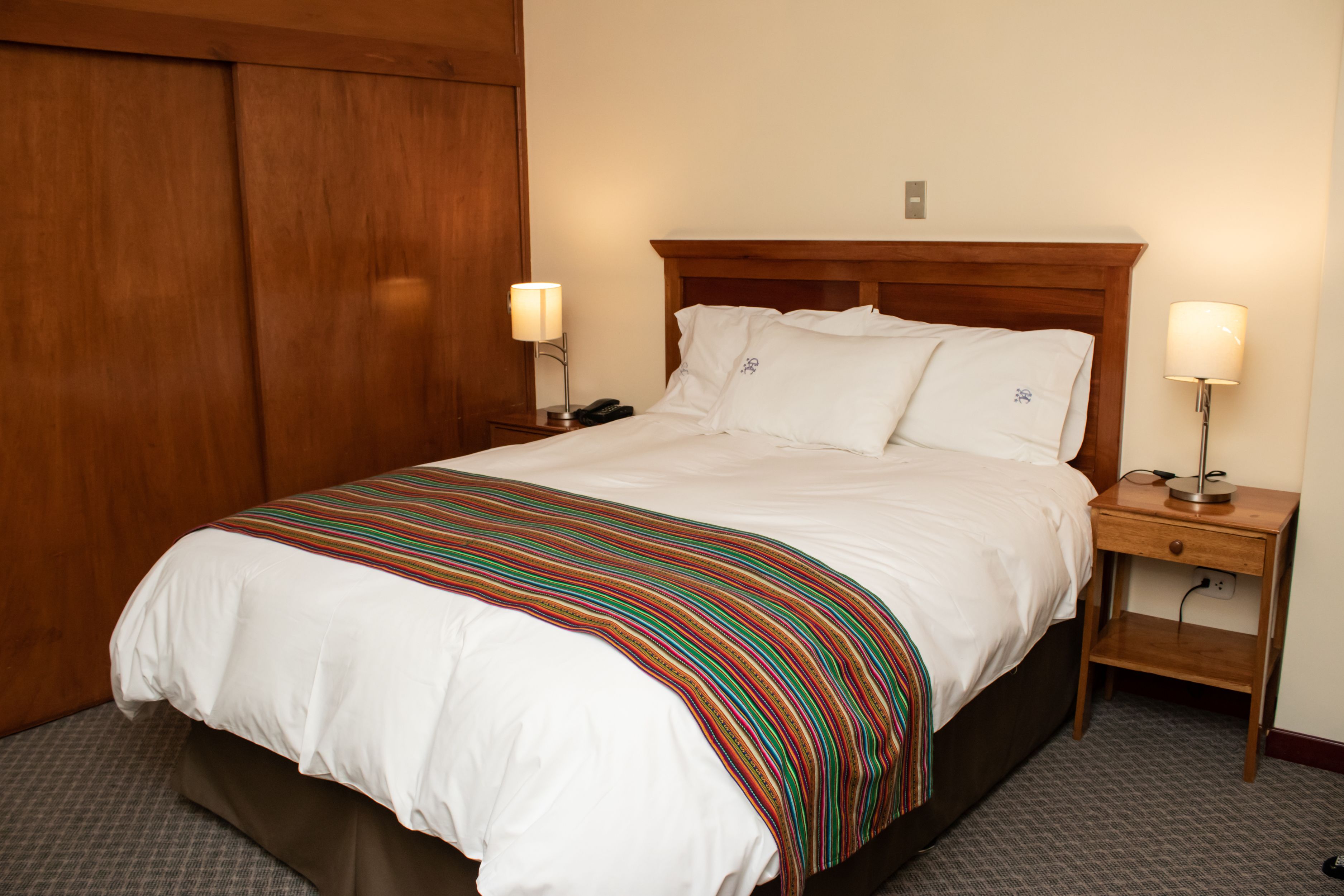 A hotel room with a large bed, wooden headboard, two bedside tables with lamps, and a wardrobe.
