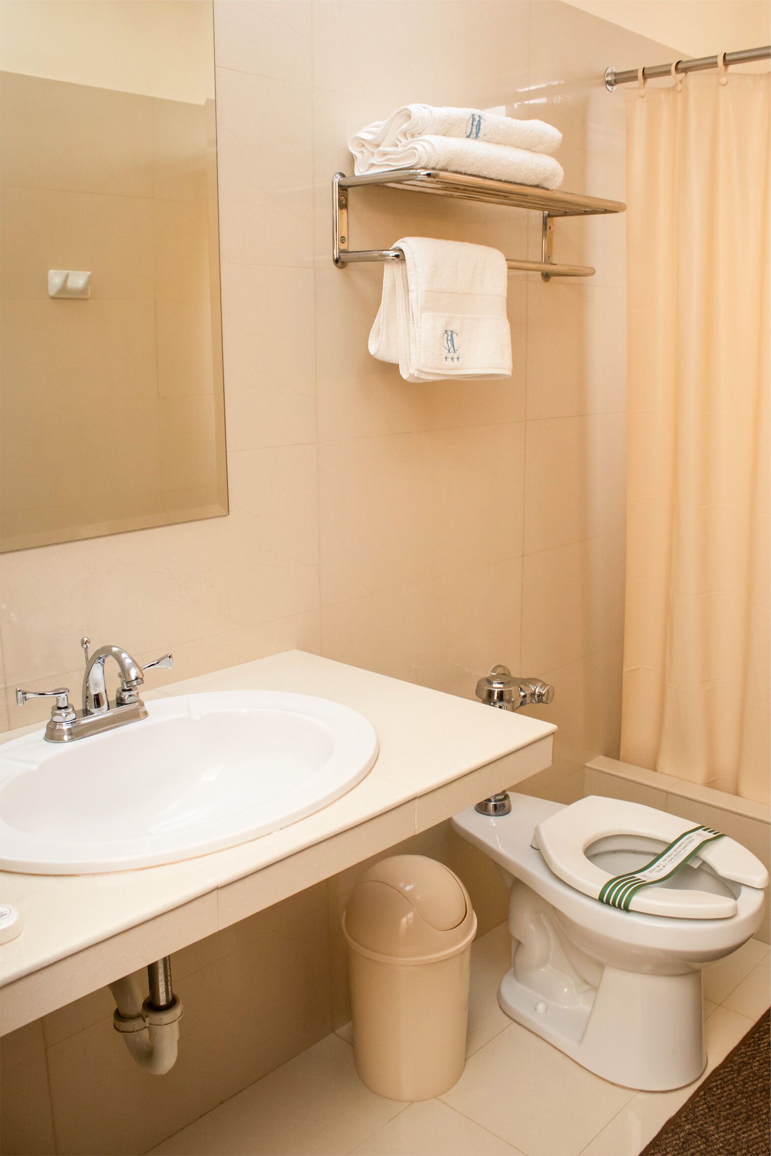 A bathroom with two sinks, a toilet, a trash bin, and a towel rack with towels.