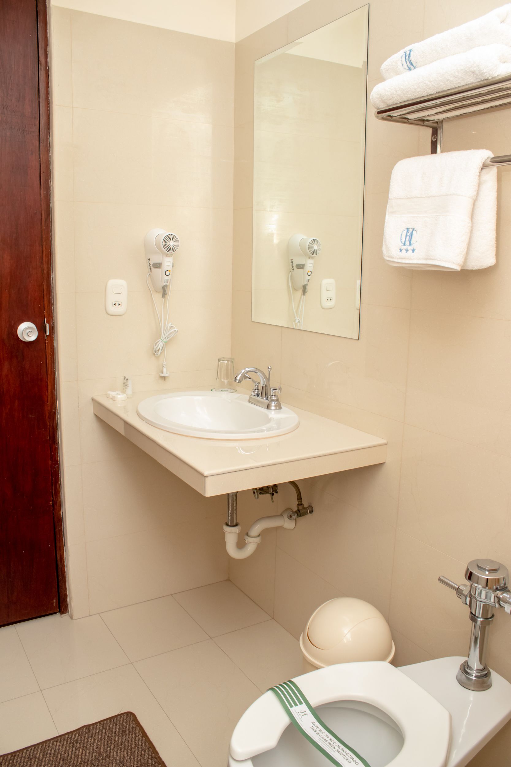 Een badkamer met een wastafel, spiegel, handdoekrek, toilet en een handdroger.