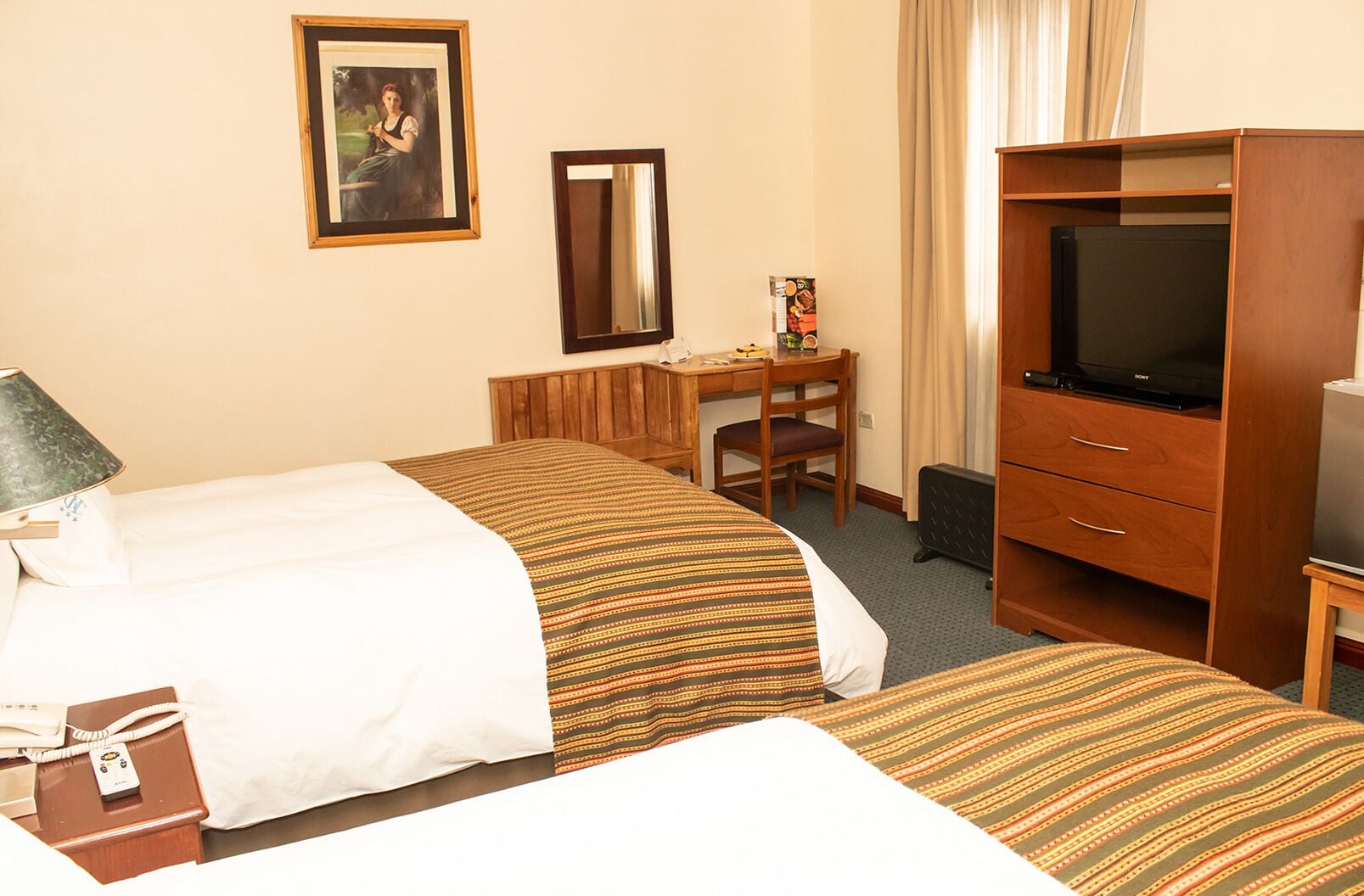 A hotel room with two beds, a desk, a chair, a television, and a telephone.