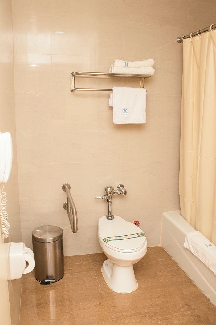 A small, clean bathroom with a toilet, a hand dryer, a trash bin, and a towel rack with folded towels.