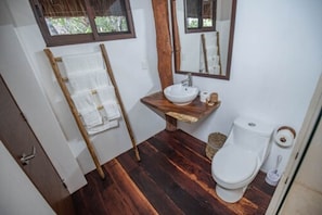 Un baño con tocador de madera, lavamanos blanco, inodoro y un espejo grande.