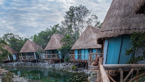 A wooden deck overlooking a calm water body with lily pads, surrounded by thatched-roof huts with blue walls. - Zamna eco-lodge Tulum (Tulum)