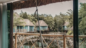A wooden deck with a hammock, overlooking a water body with thatched-roof structures. - Zamna eco-lodge Tulum (Tulum)